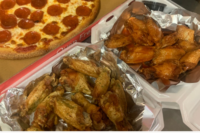 A pepperoni pizza beside two trays of hot wings, mild and buffalo